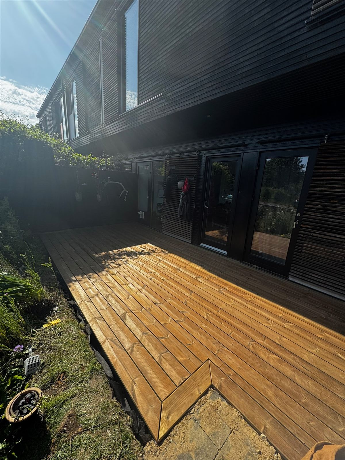 Nylagt terrasse i thermofyr i solen op til mørkt hus