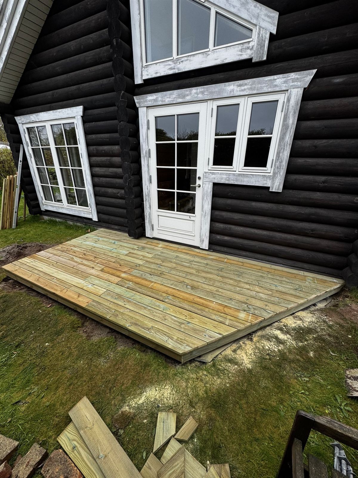 Ny terrasse i trykimprægneret træ op til sort bjælkehytte