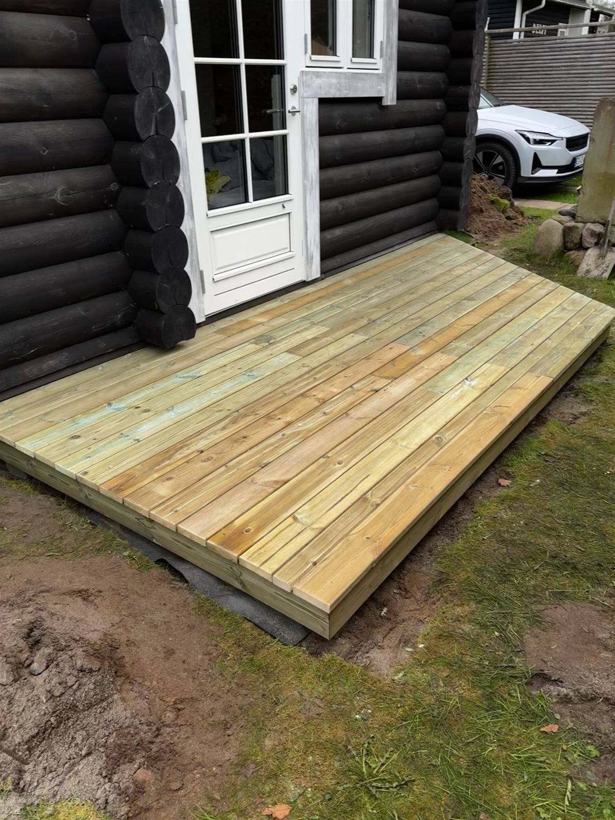 Ny terrasse i trykimprægneret træ op til sort bjælkehytte